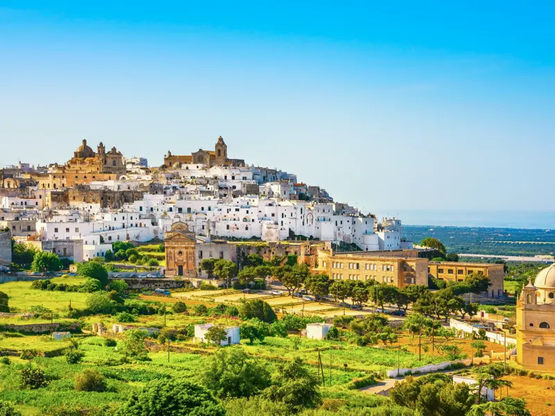 Die weiße Stadt Ostuni thront auf einem Hügel in Apulien, umgeben von grüner Landschaft und mit Blick auf die Küste.
