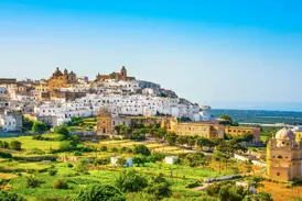 Die weiße Stadt Ostuni thront auf einem Hügel in Apulien, umgeben von grüner Landschaft und mit Blick auf die Küste.