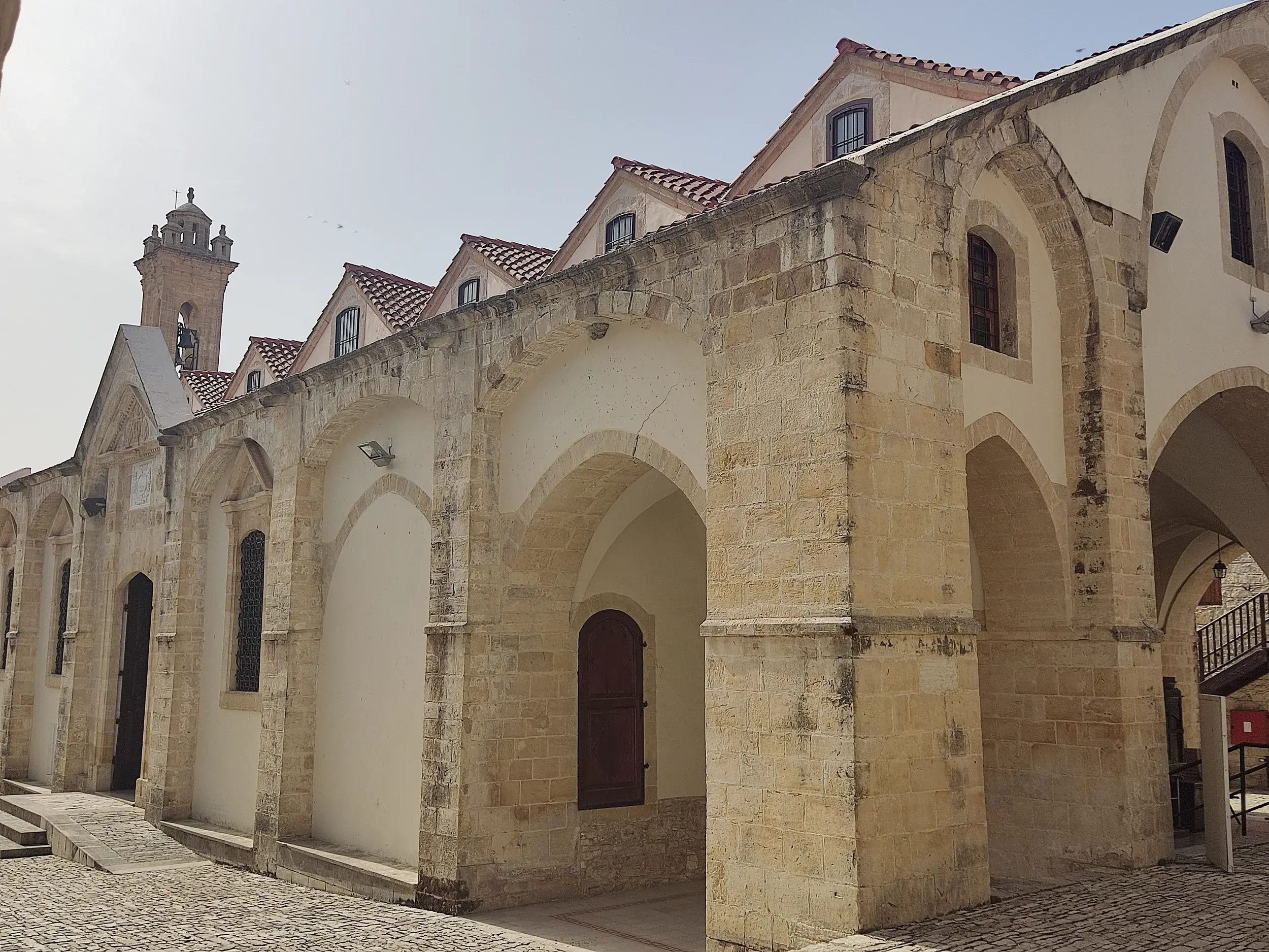 Byzantinische Lazarus-Kirche in Larnaka mit steinernem Arkadengang, roten Ziegeldächern und Glockenturm bei Sonnenschein.