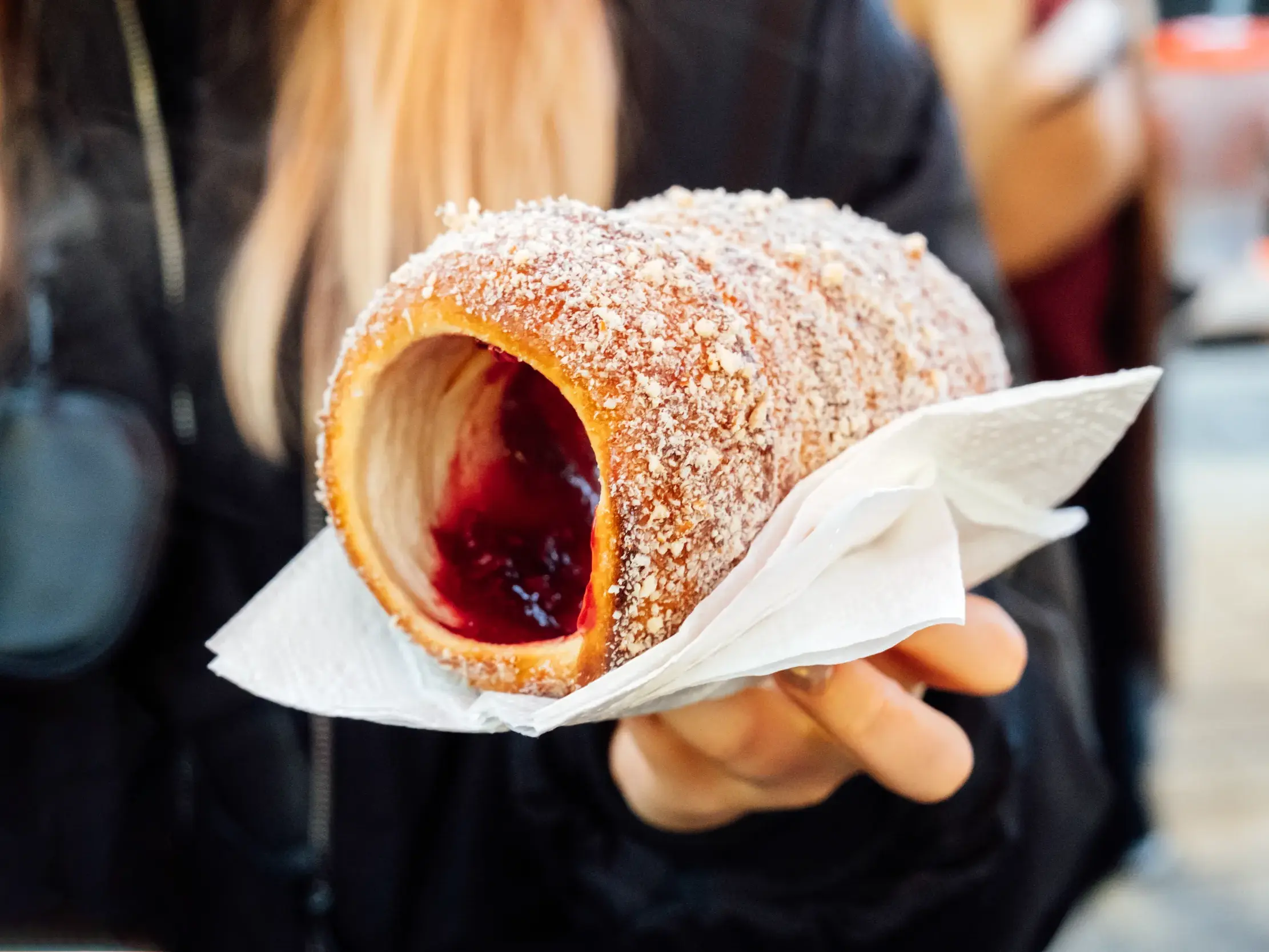 Eine Hand hält einen frischen ungarischen Baumstriezel mit Marmelade, eine kulinarische Spezialität aus Budapest.