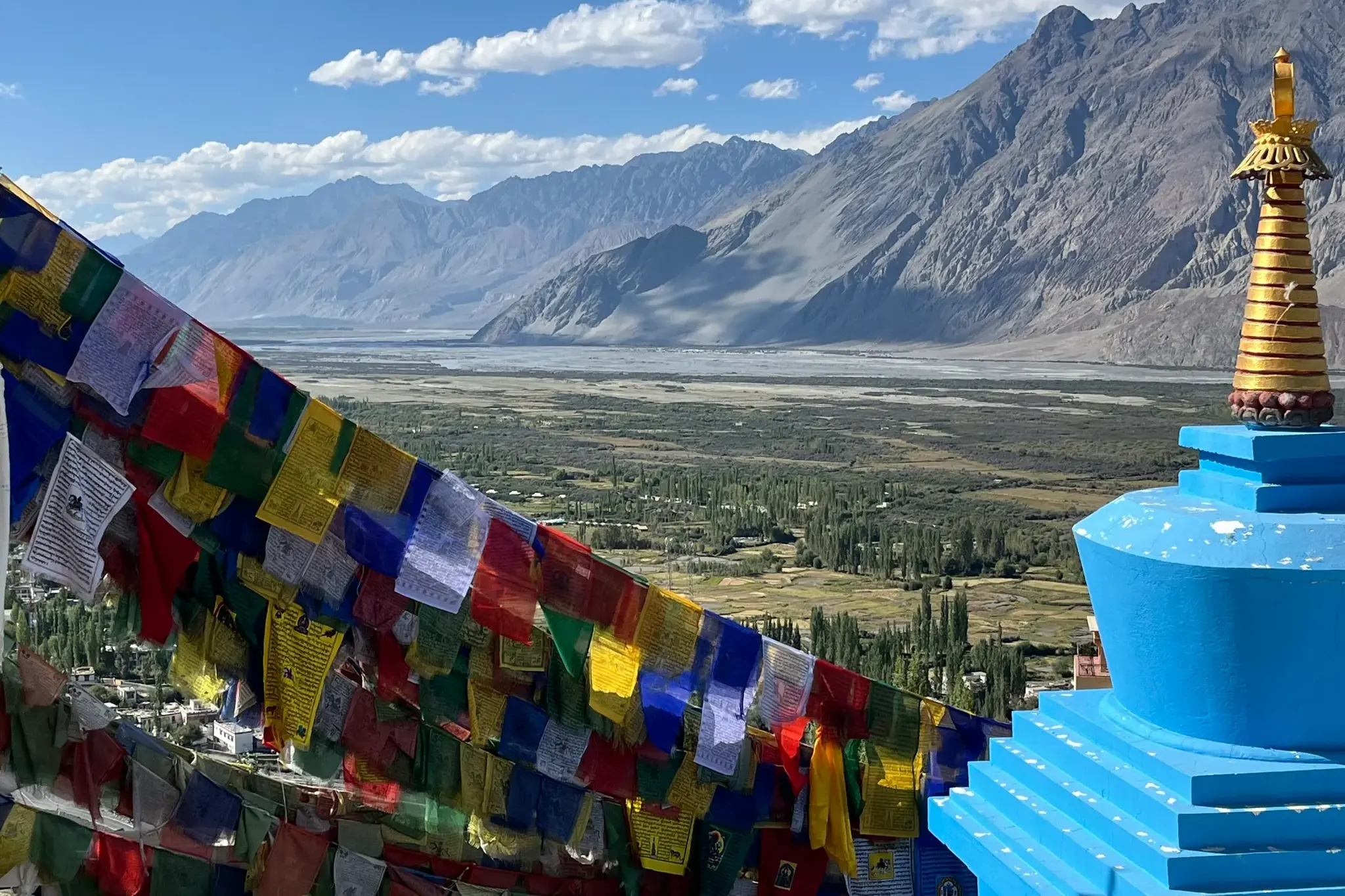 Bunte Gebetsfahnen und ein Stupa am Diskit-Kloster mit weitem Blick über das grüne Nubra-Tal und die Berge Ladakhs.