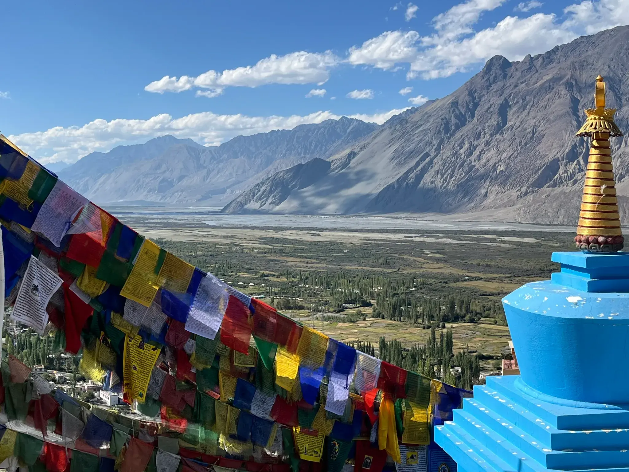 Bunte Gebetsfahnen und ein Stupa am Diskit-Kloster mit weitem Blick über das grüne Nubra-Tal und die Berge Ladakhs.
