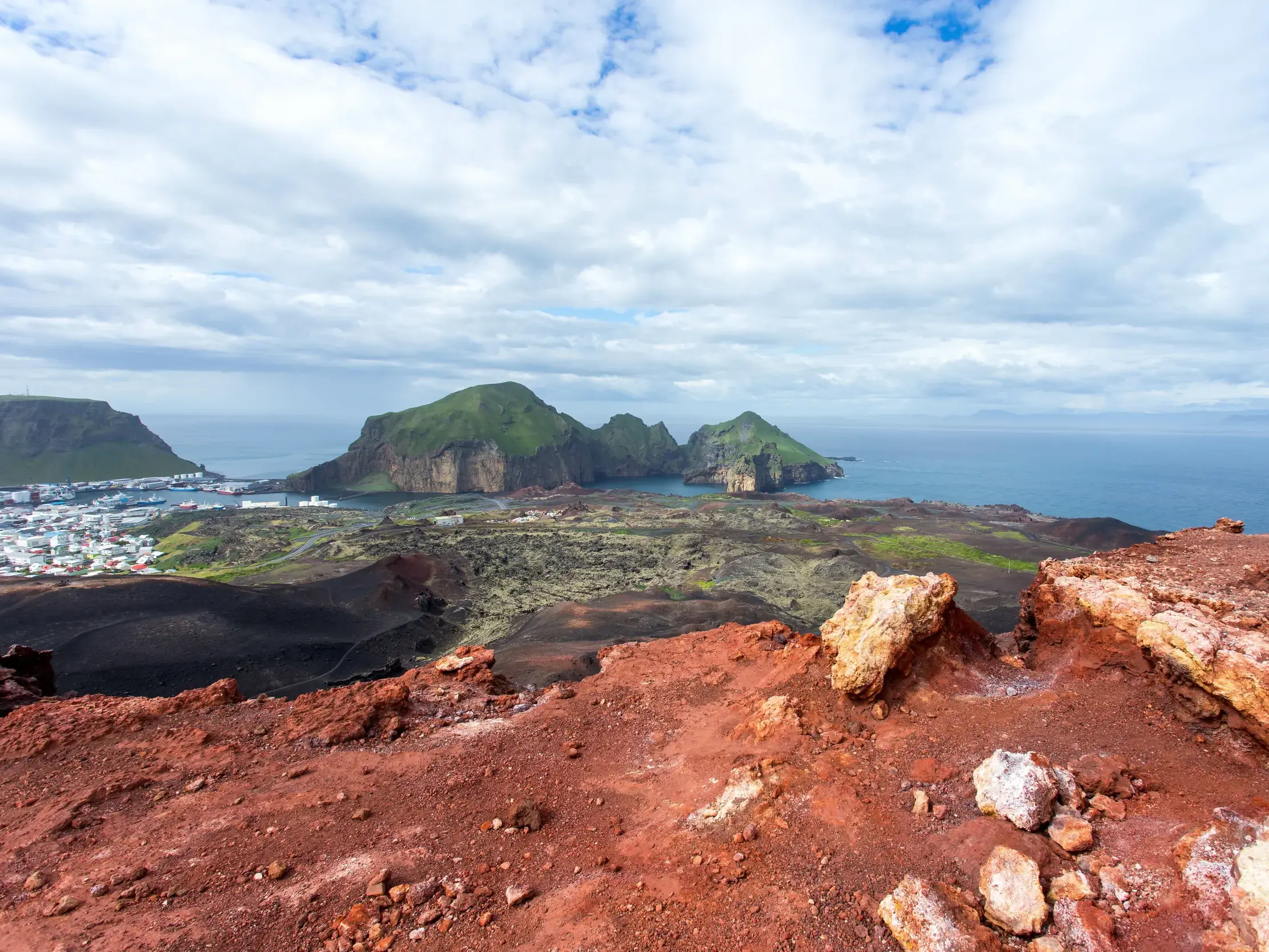 Aussicht beim Wandern auf einem Vulkankrater über die Stadt Heimaey und die zerklüfteten Westmännerinseln in Island.