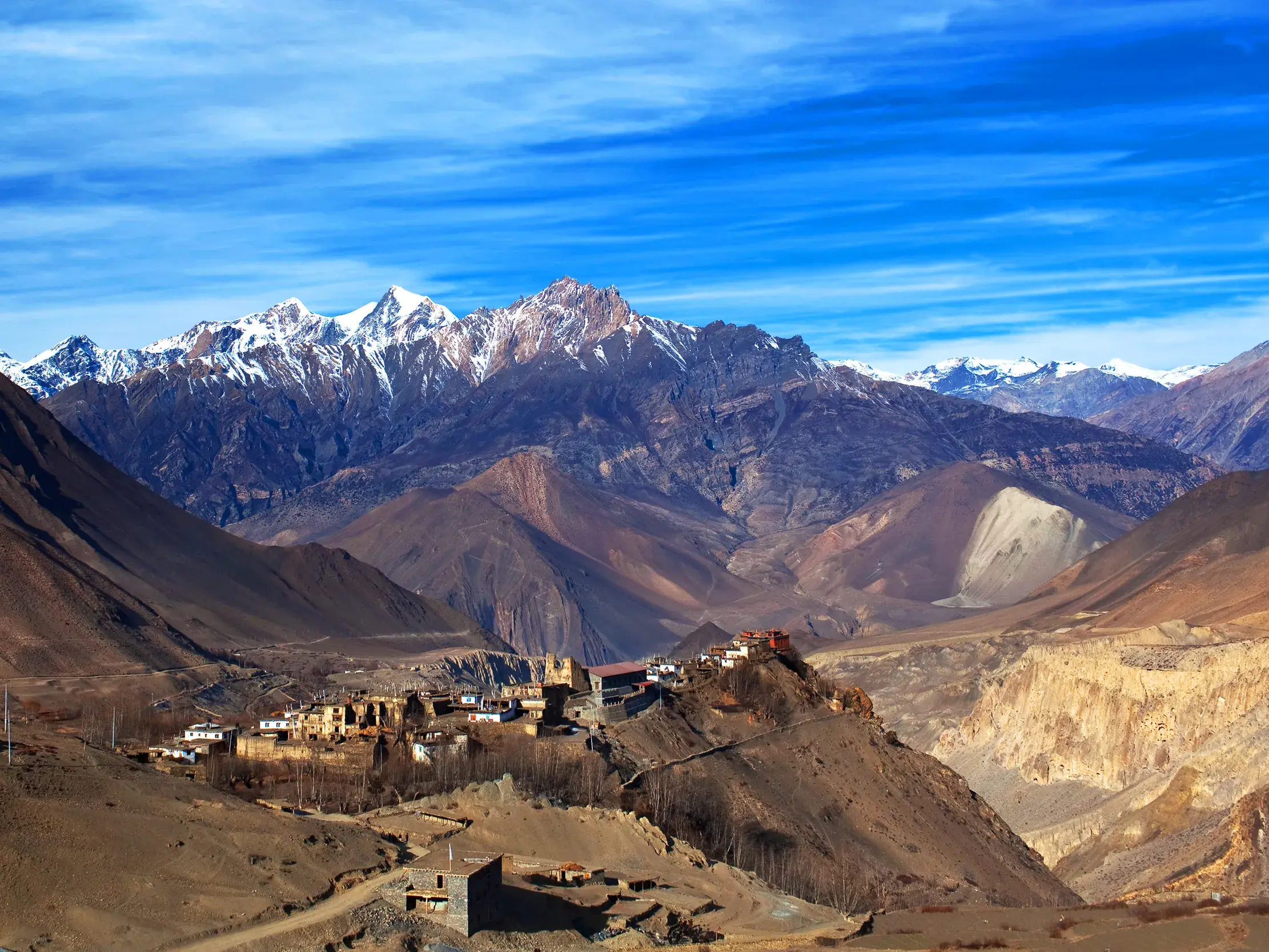 Panoramablick auf das Bergdorf Kagbeni in der kargen Landschaft von Mustang vor dem schneebedeckten Nilgiri-Massiv in Nepal.