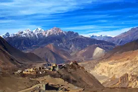 Panoramablick auf das Bergdorf Kagbeni in der kargen Landschaft von Mustang vor dem schneebedeckten Nilgiri-Massiv in Nepal.