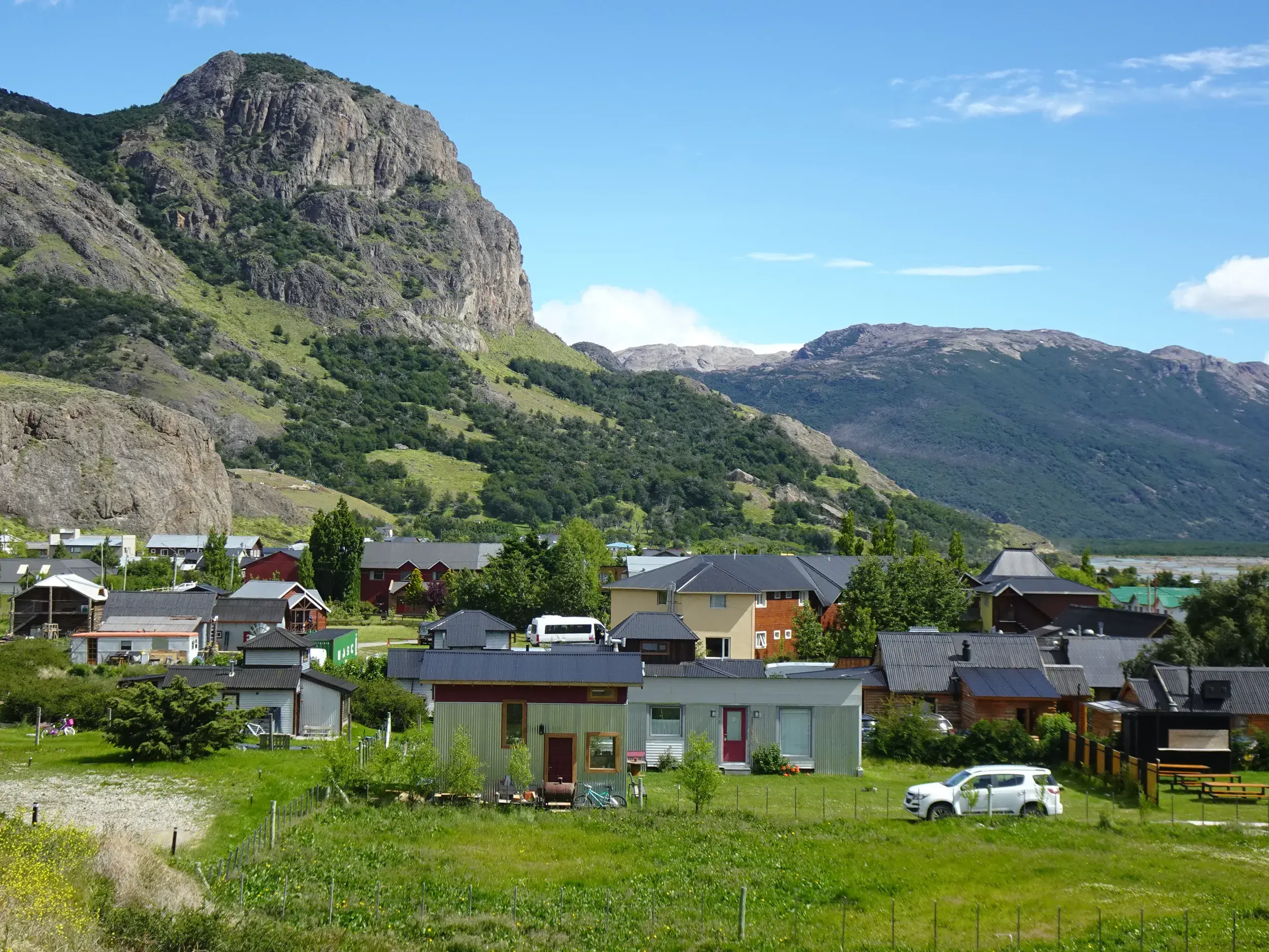 Panoramablick auf das argentinische Trekking-Dorf El Chaltén, das sich in einem grünen Tal vor hohen, schroffen Bergen ausbreitet.