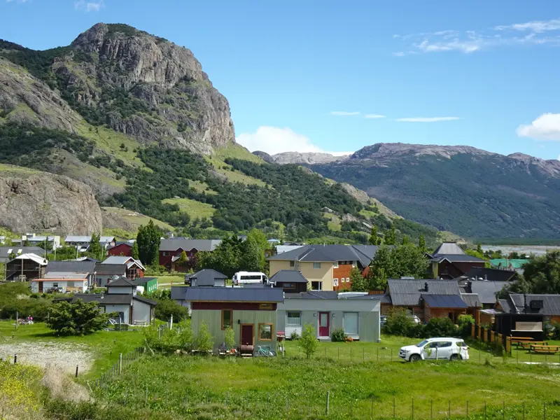 Panoramablick auf das argentinische Trekking-Dorf El Chaltén, das sich in einem grünen Tal vor hohen, schroffen Bergen ausbreitet.