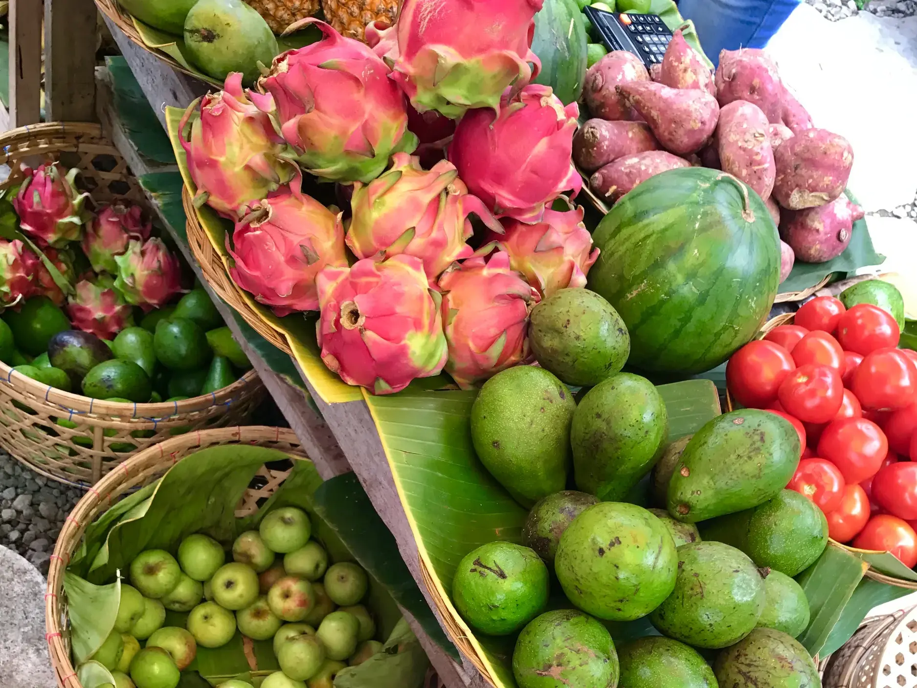 Farbenfrohe, exotische Früchte wie Drachenfrüchte, Avocados und Tomaten in Weidenkörben auf einem Marktstand in Indonesien.