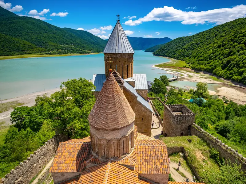 Die historische Wehrkirche Ananuri thront über dem türkisblauen Aragwi-Stausee in den grünen Bergen des Kaukasus in Georgien.