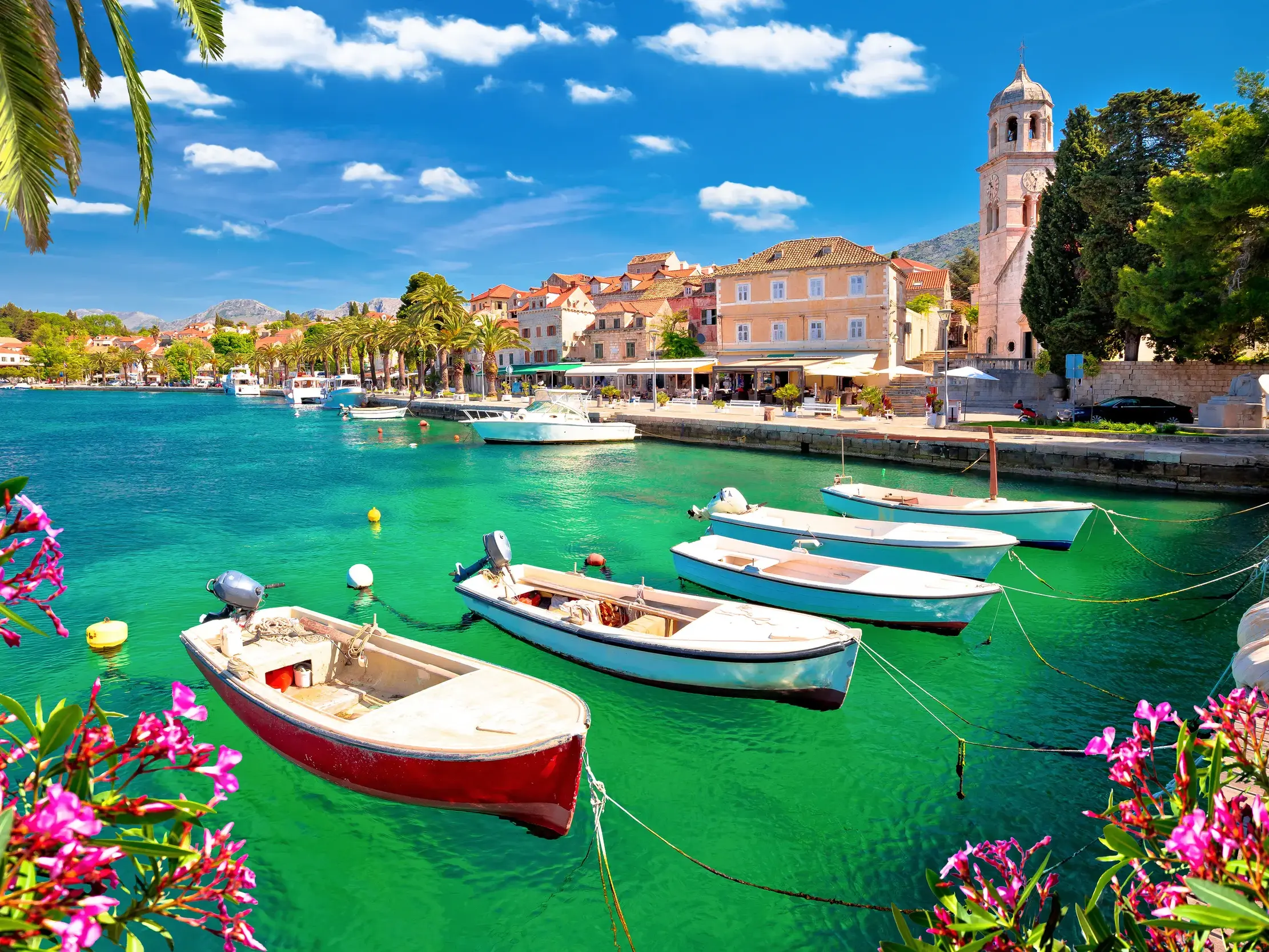 Malerischer Hafen von Cavtat mit bunten Booten im smaragdgrünen Wasser der Adria unter blauem Himmel mit Wolken.
