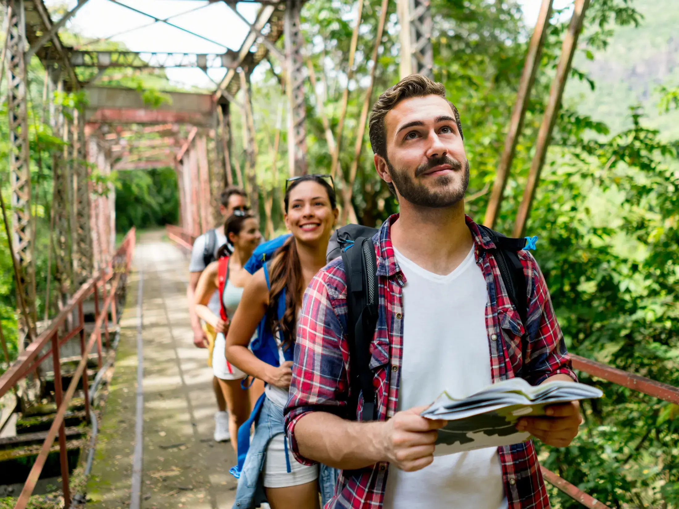 Eine junge Reisegruppe mit Rucksäcken überquert eine Stahlbrücke auf einer Wanderung durch das Mandor-Tal in Peru.