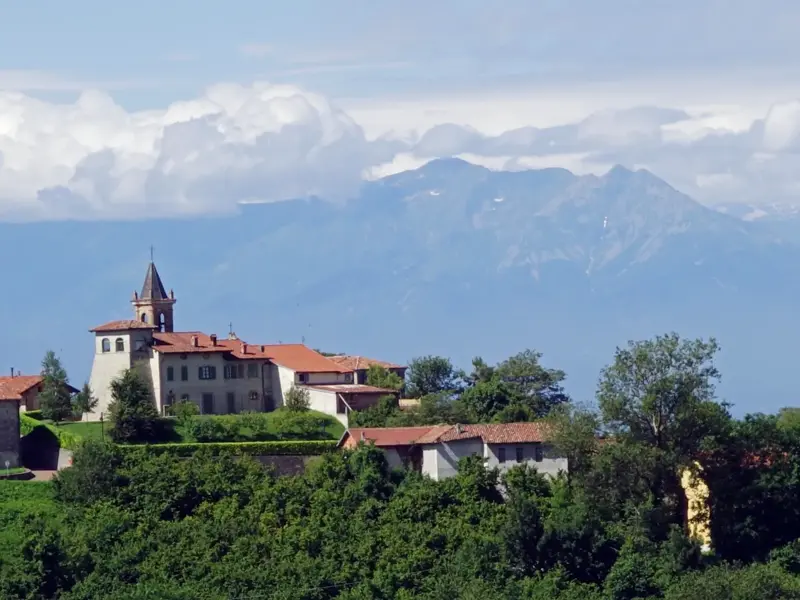 Idyllisches Hügeldorf in der Langhe, eingebettet in grüne Wälder, mit Panoramablick auf die Alpenkette im Piemont.