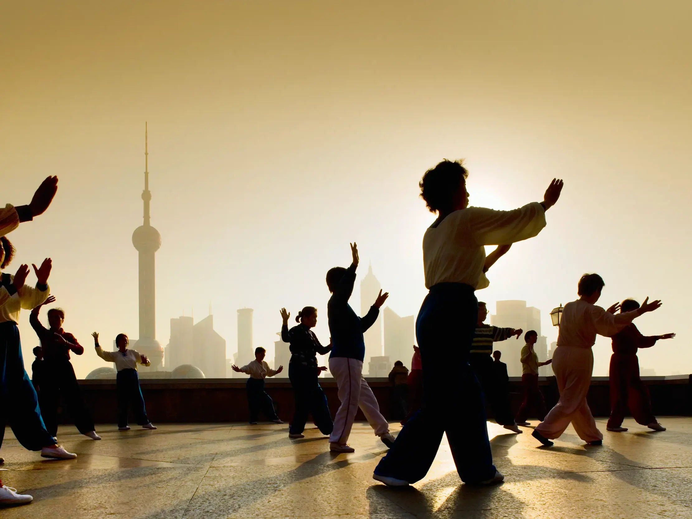 Gruppe bei Tai-Chi-Übungen am Uferboulevard Bund in Shanghai im Gegenlicht mit Blick auf die Pudong-Skyline am Morgen.