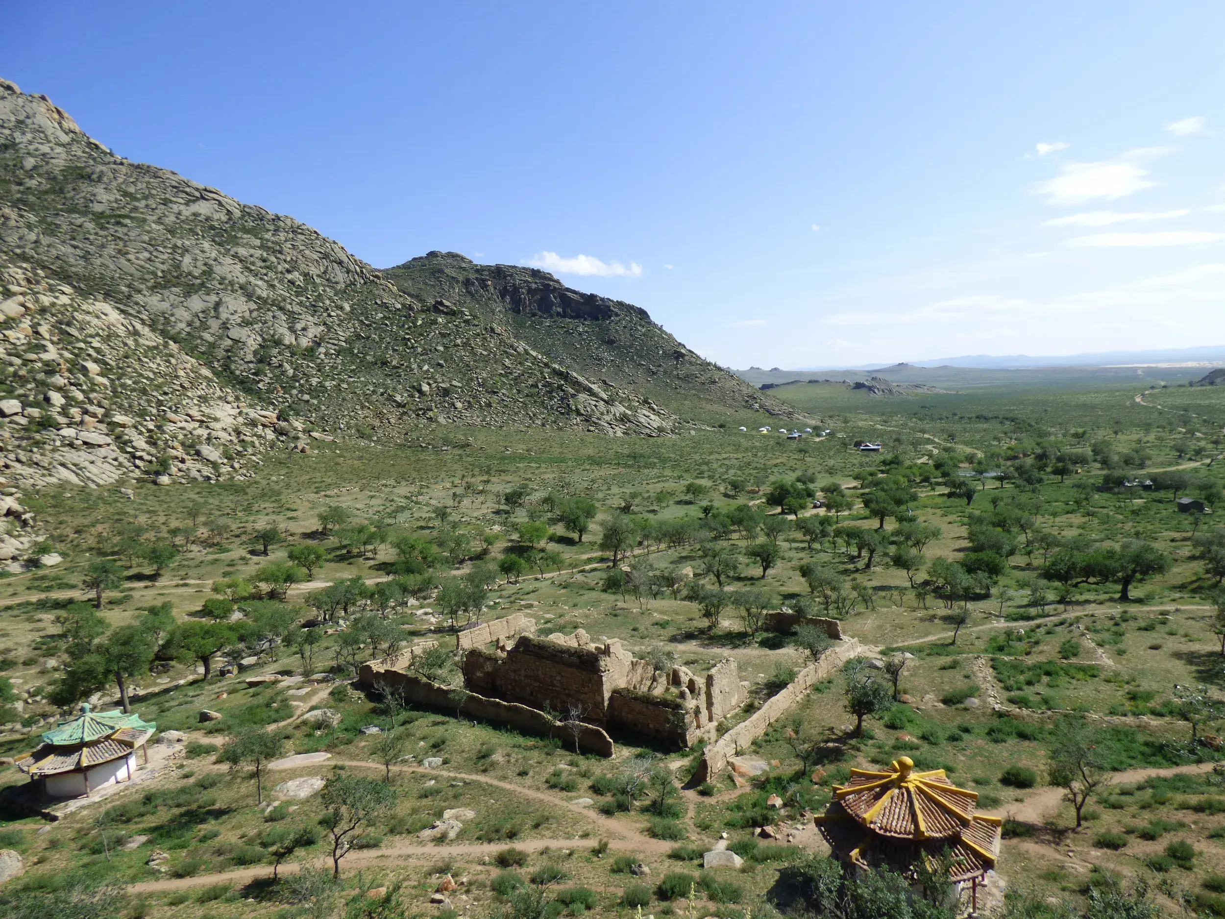 Blick von den Felsen des Khugnu Khan-Gebirges auf die Klosterruinen Erdene Hamba in der weiten, grünen Steppe der Mongolei.