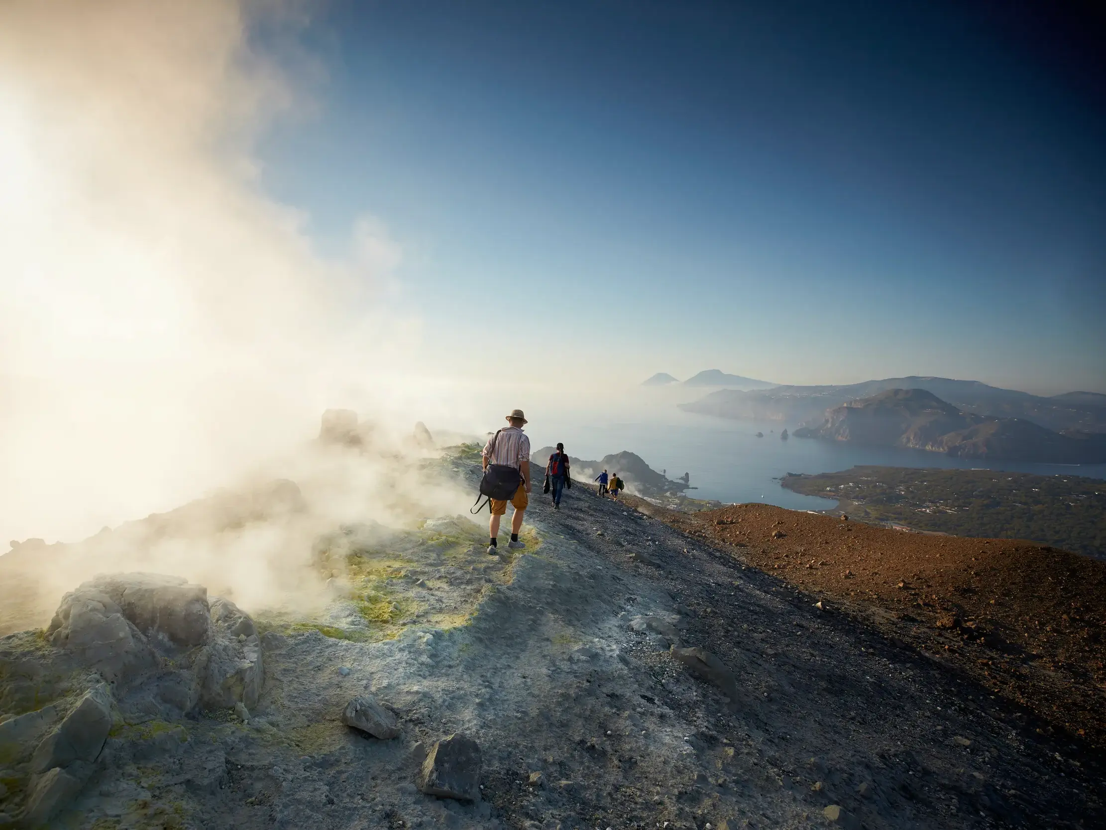 Eine Reisegruppe wandert entlang des dampfenden, schwefelgelben Kraterrands des Gran Cratere auf der Insel Vulcano.