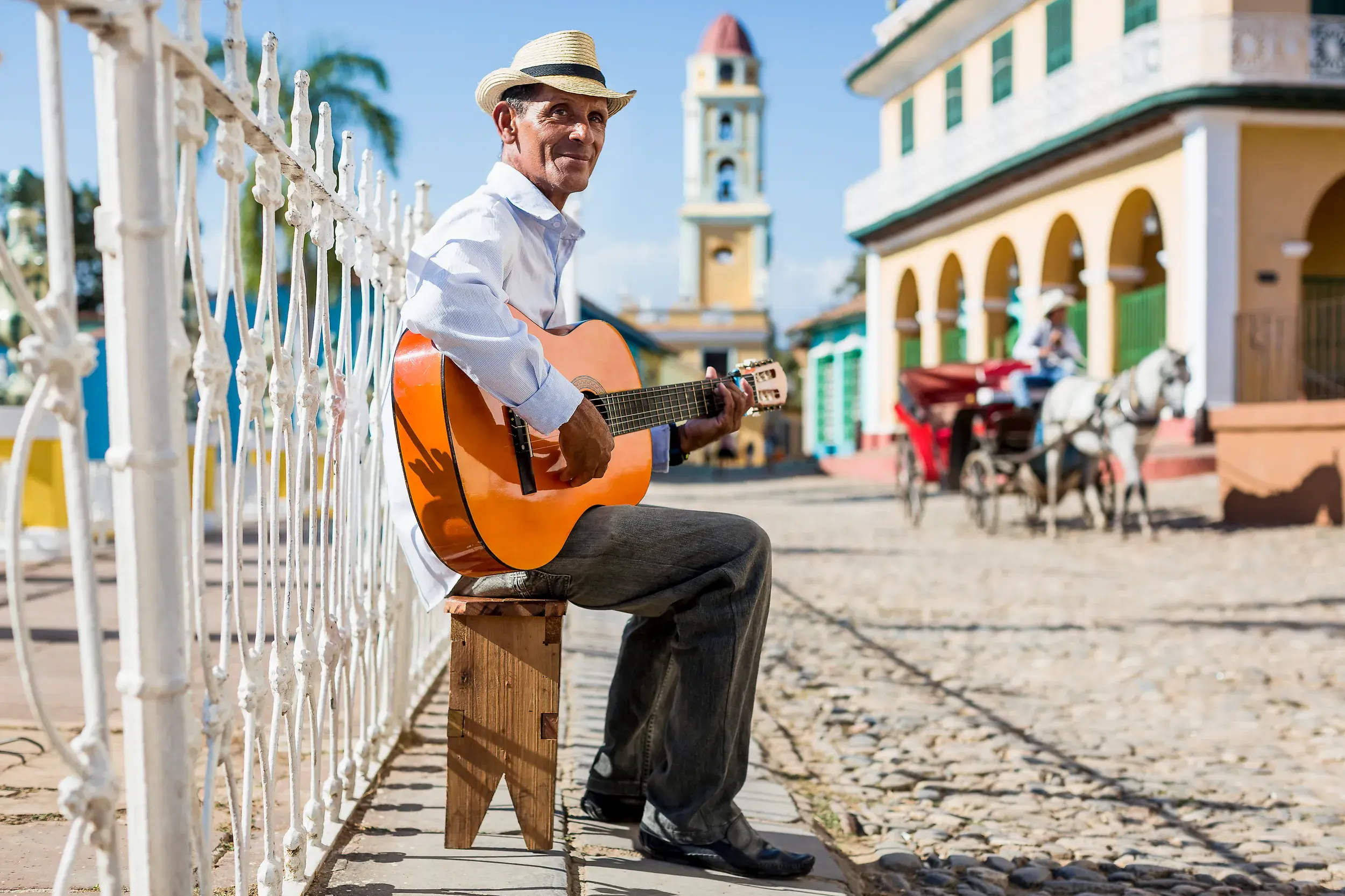 Einheimischer Musiker spielt Gitarre auf einer Straße in Trinidad, im Hintergrund der Glockenturm von San Francisco de Asís.