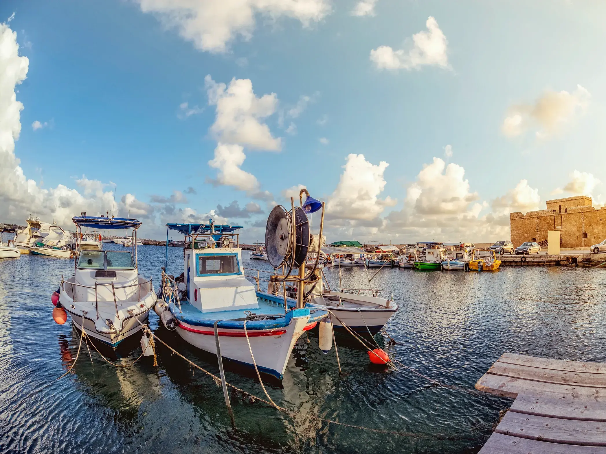 Zahlreiche Fischerboote am Pier im Hafen von Paphos auf Zypern, im Hintergrund das historische Kastell bei warmem Abendlicht.