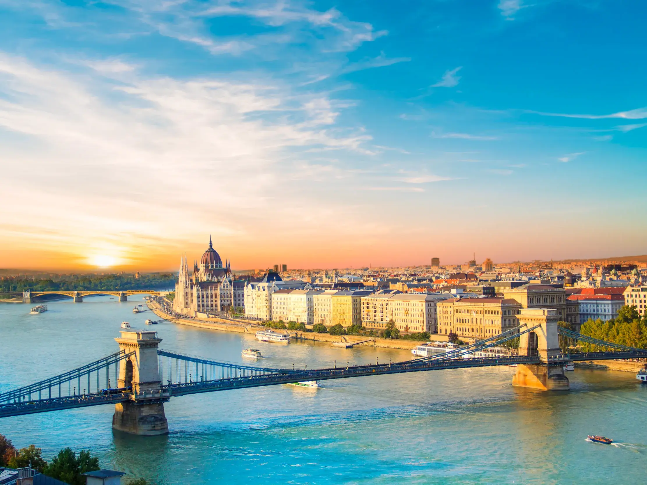Stimmungsvoller Sonnenuntergang über Budapest mit der Kettenbrücke im Vordergrund und dem Parlament am Ufer der Donau.