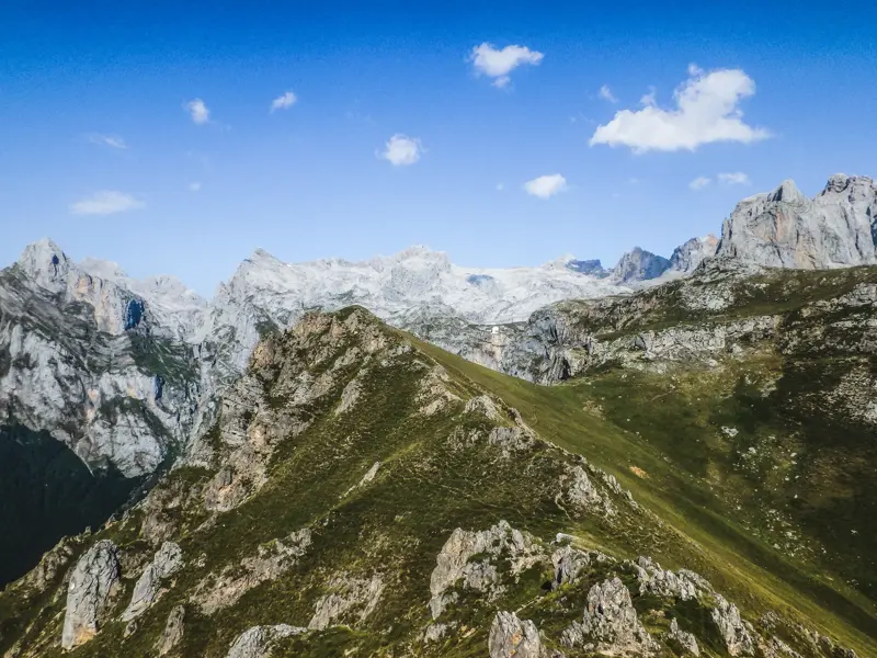 Ein schmaler Pfad auf einem grünen Grat beim Trekking in den Picos de Europa mit Blick auf die Kalkstein-Gipfel Asturiens.
