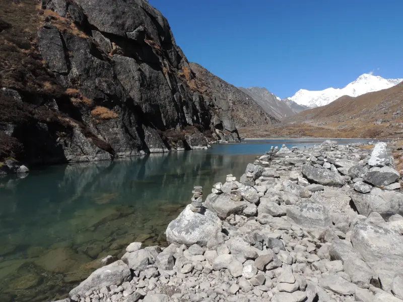 Steinmännchen am Ufer des türkisen Gokyo-Sees in Nepal, im Hintergrund erheben sich die schneebedeckten Gipfel des Himalaya.