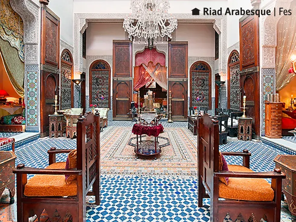 Innenhof Ihres Hotels Riad Arabesque in Fes mit blau-weißen Mosaikfliesen, Holzschnitzereien und einem Kronleuchter.