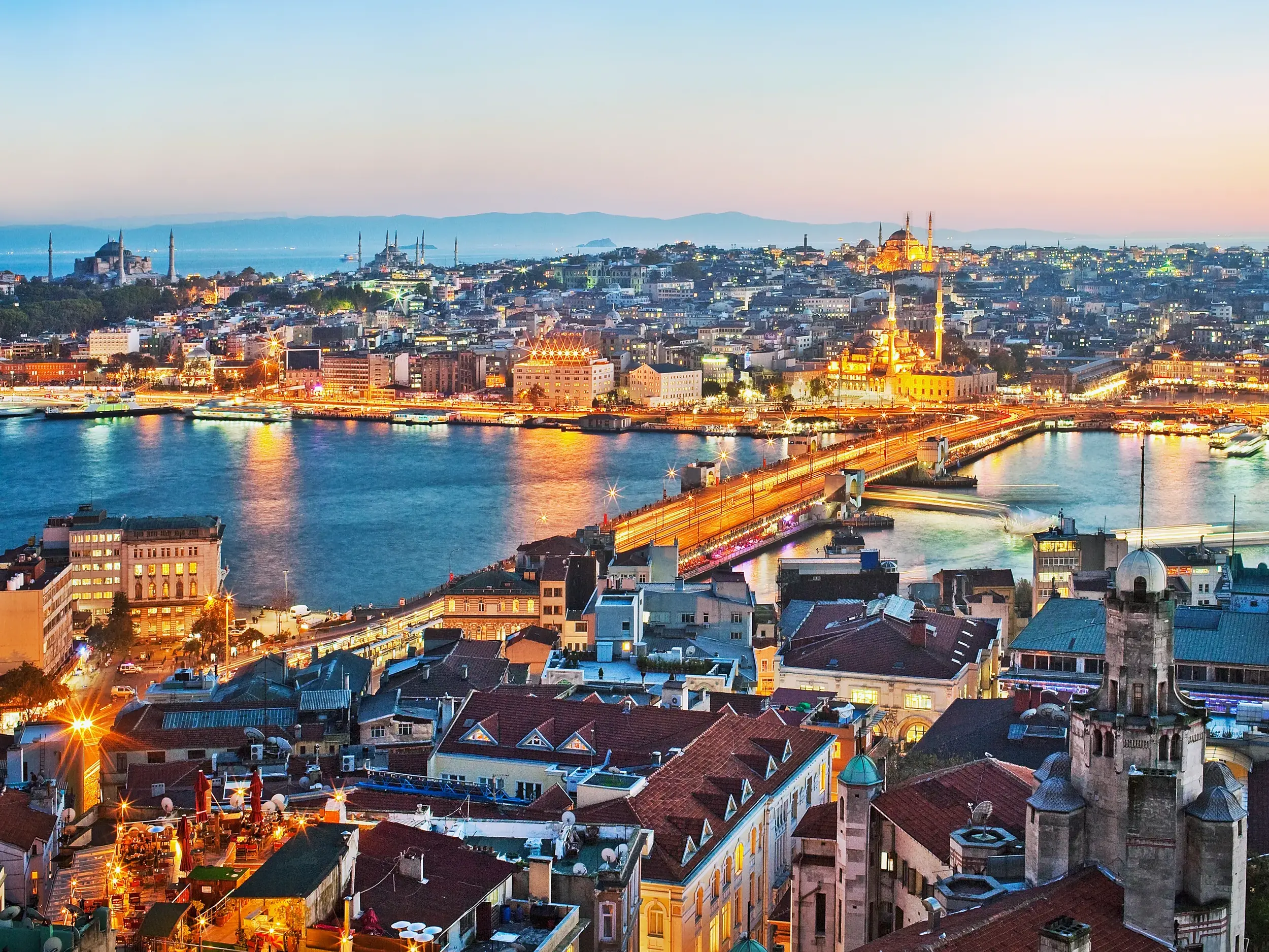 Abendlicher Panoramablick über Istanbul mit Brücke über den Bosporus, im Hintergrund die beleuchtete Hagia Sophia und Blaue Moschee.