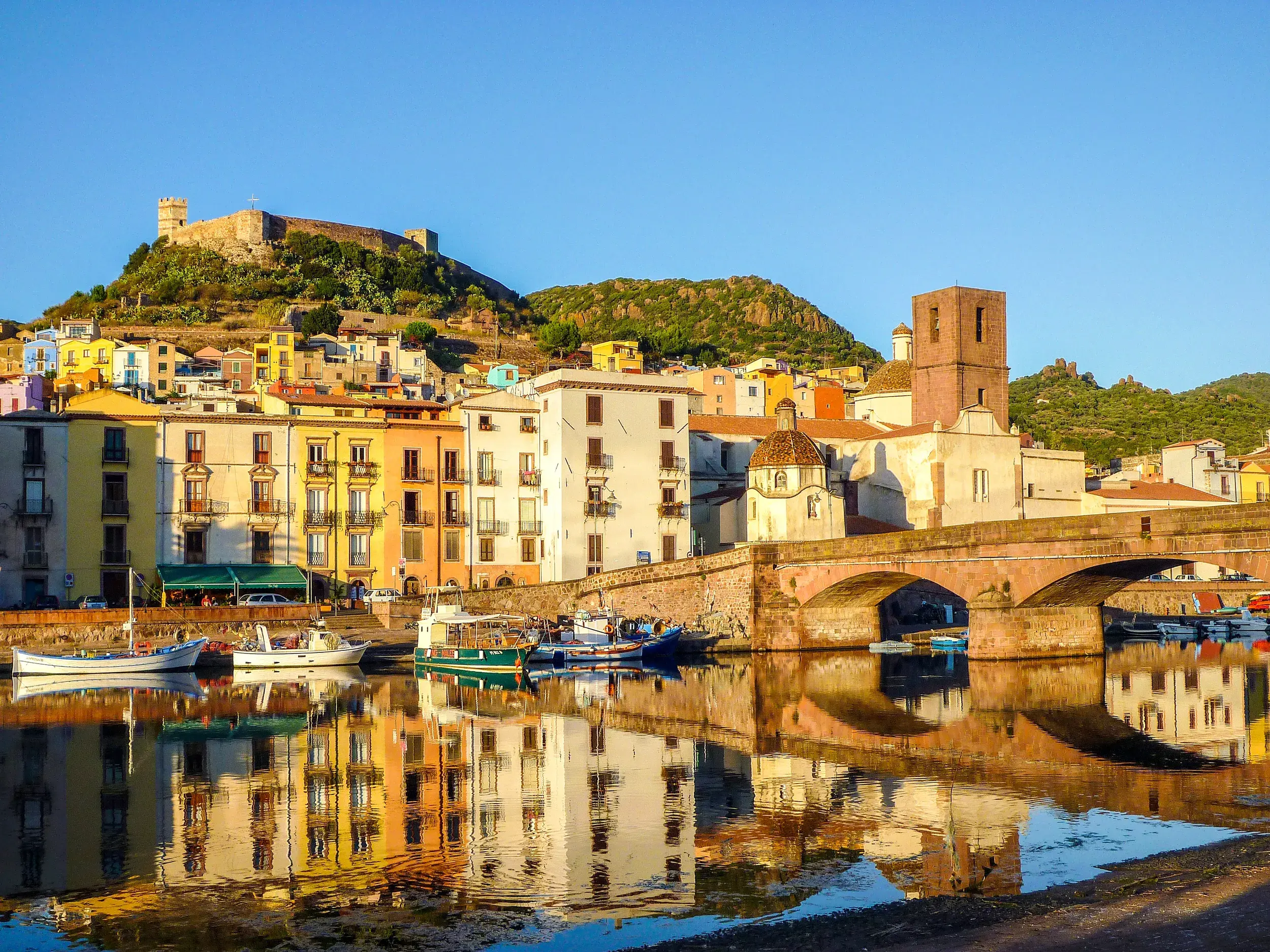 Die bunten Häuser und die historische Ponte Vecchio von Bosa auf Sardinien spiegeln sich bei Sonnenaufgang im Fluss Temo.