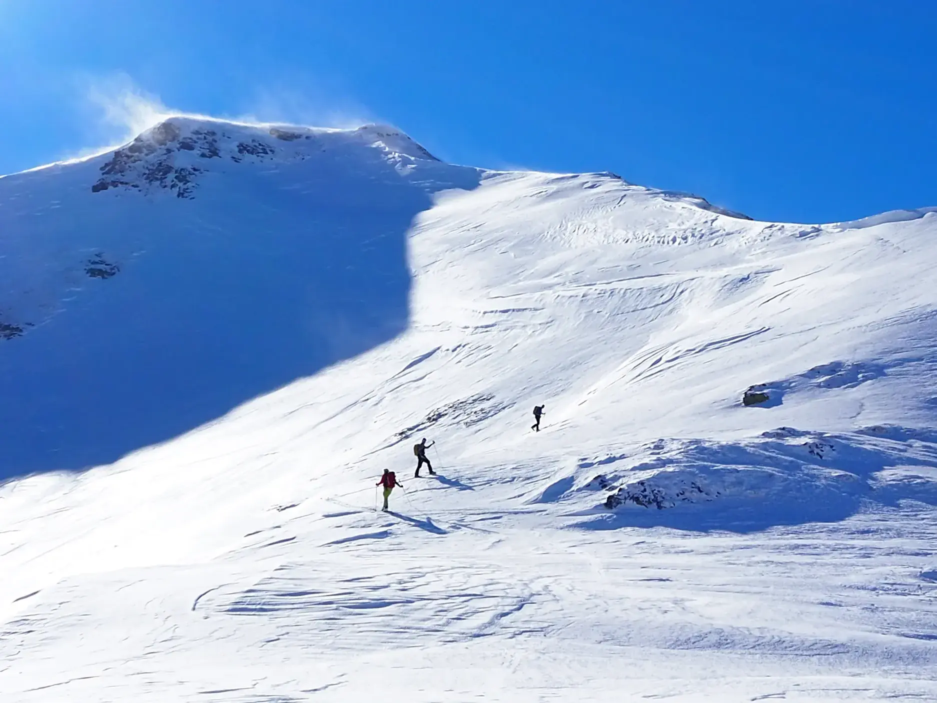 Drei Skitourengeher auf dem Weg zum windigen Gipfel des Korab in den albanischen Alpen bei strahlend blauem Himmel.