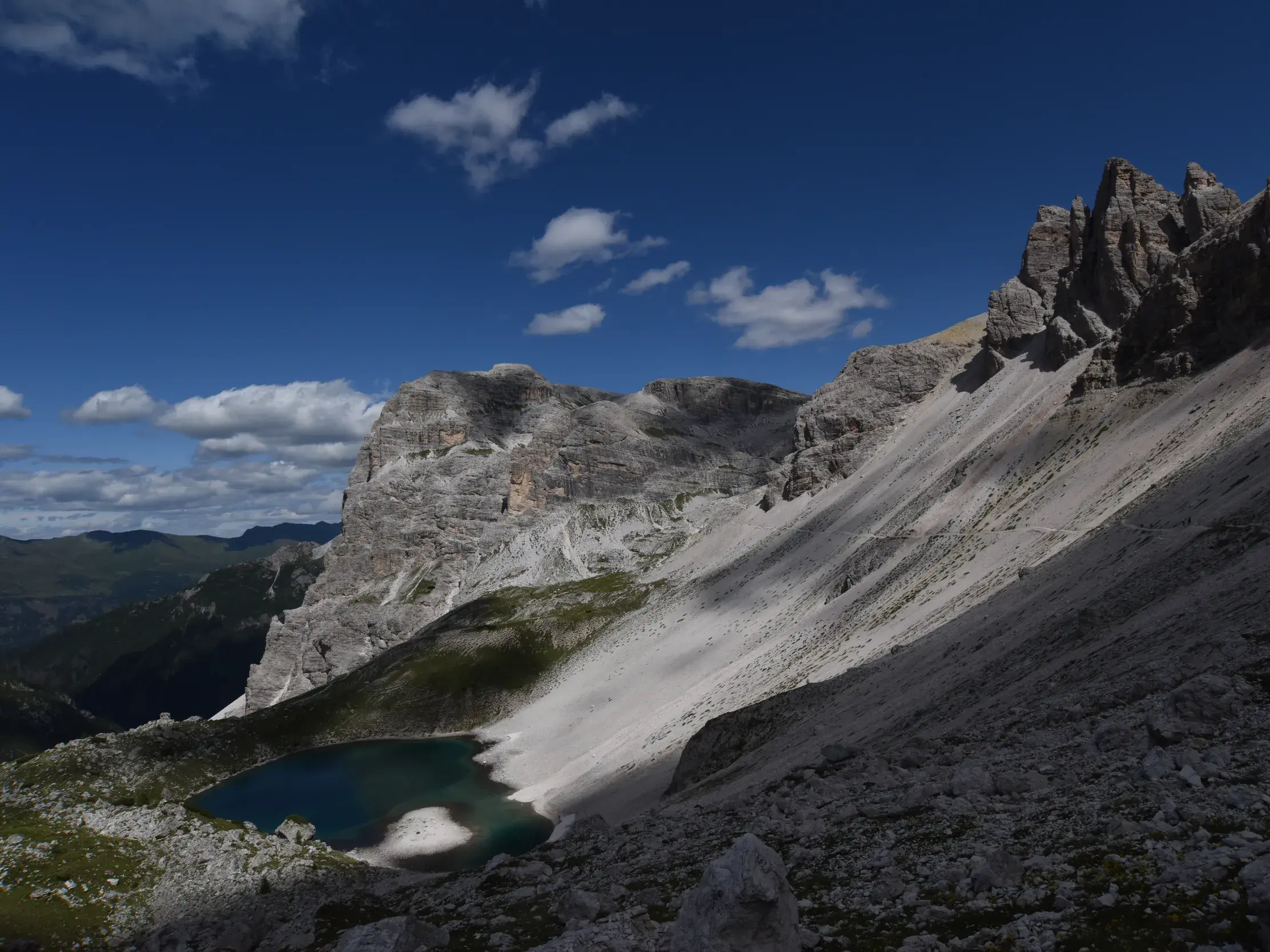 Ein Wanderweg führt über einen steilen Geröllhang der Sella-Gruppe zum tiefblauen Bergsee Lago de Pisciadù in den Dolomiten.