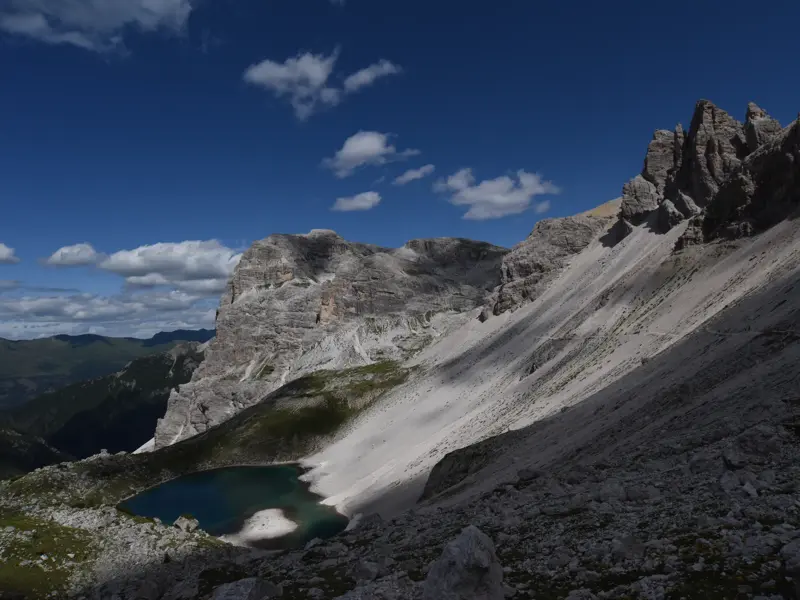 Ein Wanderweg führt über einen steilen Geröllhang der Sella-Gruppe zum tiefblauen Bergsee Lago de Pisciadù in den Dolomiten.
