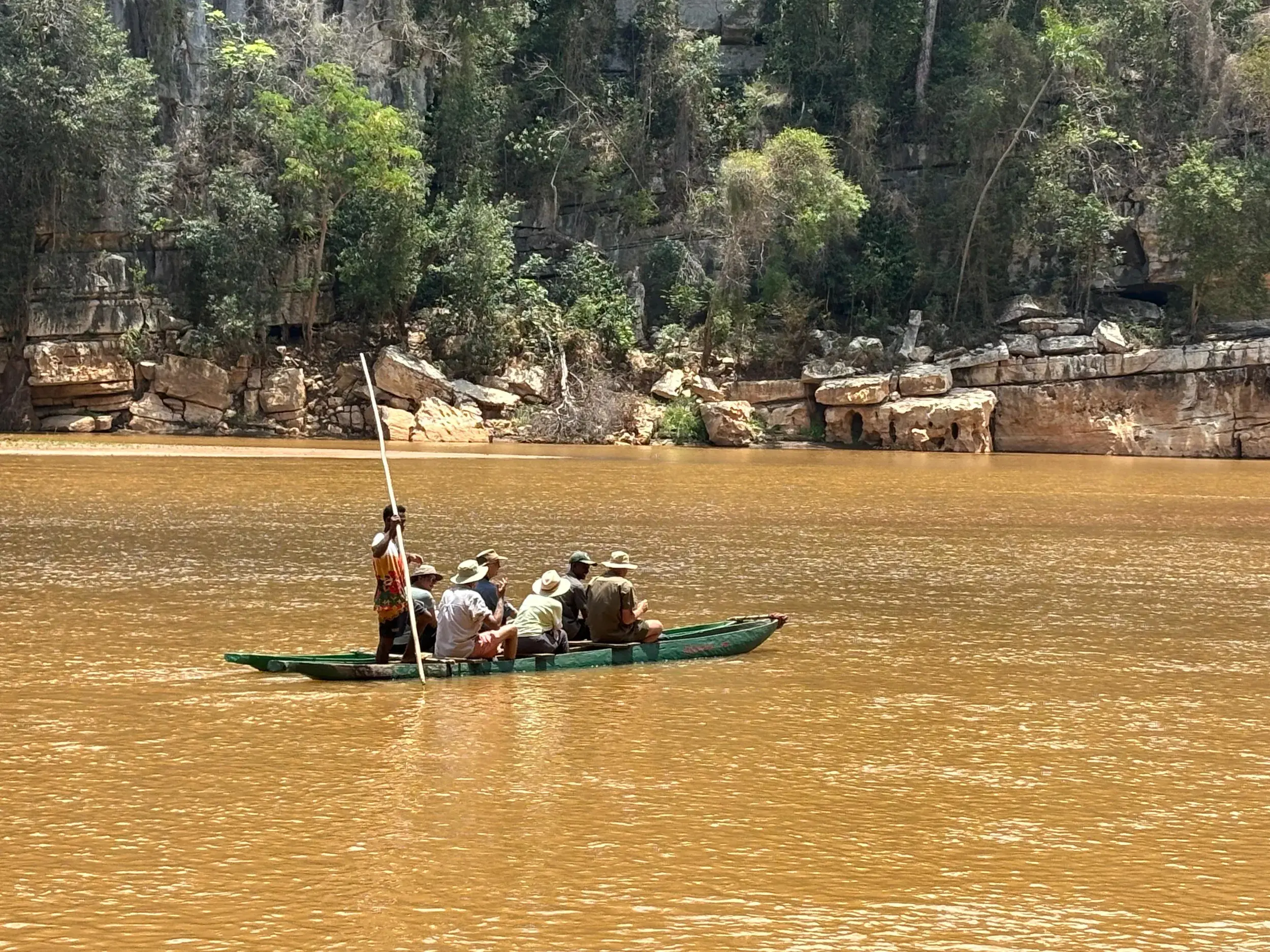 Eine Reisegruppe in einer Piroge auf dem Manambolo Fluss in Madagaskar, während ein Guide das Boot entlang der Felsklippen steuert.