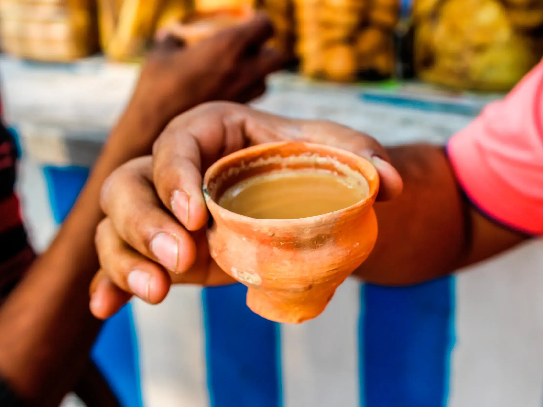 Nahaufnahme einer Hand, die eine traditionelle indische Tontasse, einen Kulhad, gefüllt mit würzigem Masala Chai Tee hält.