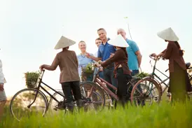 Eine Kleingruppe von Reisenden spricht mit Bäuerinnen in Kegelhüten während einer Radtour durch die grünen Felder von Tra Que.