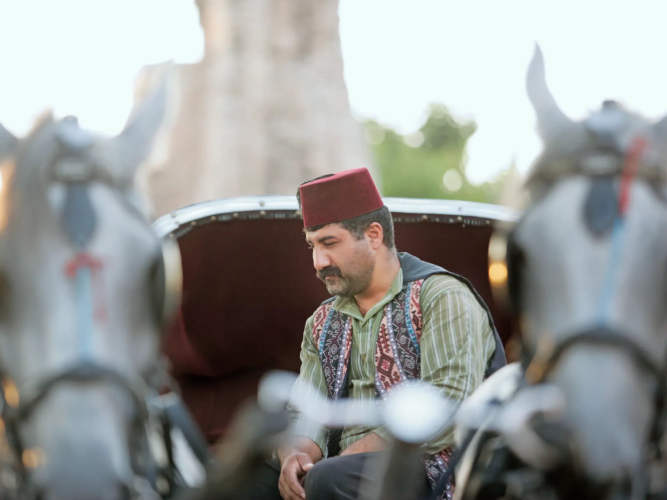 Ein Kutscher in traditioneller Kleidung mit rotem Fes sitzt im Abendlicht nachdenklich auf dem Bock einer Pferdekutsche in Istanbul.
