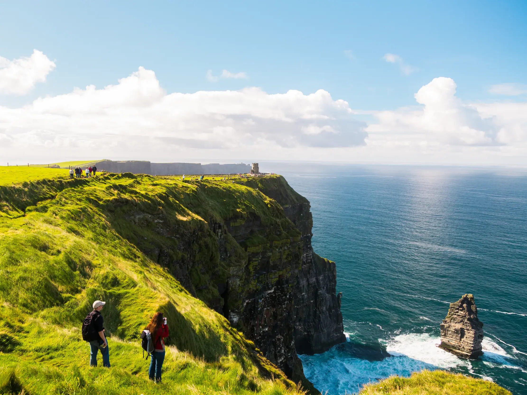 Wanderer auf einer Studienreise entlang der grünen Klippen von Moher mit weitem Blick auf den Atlantik in Irland.