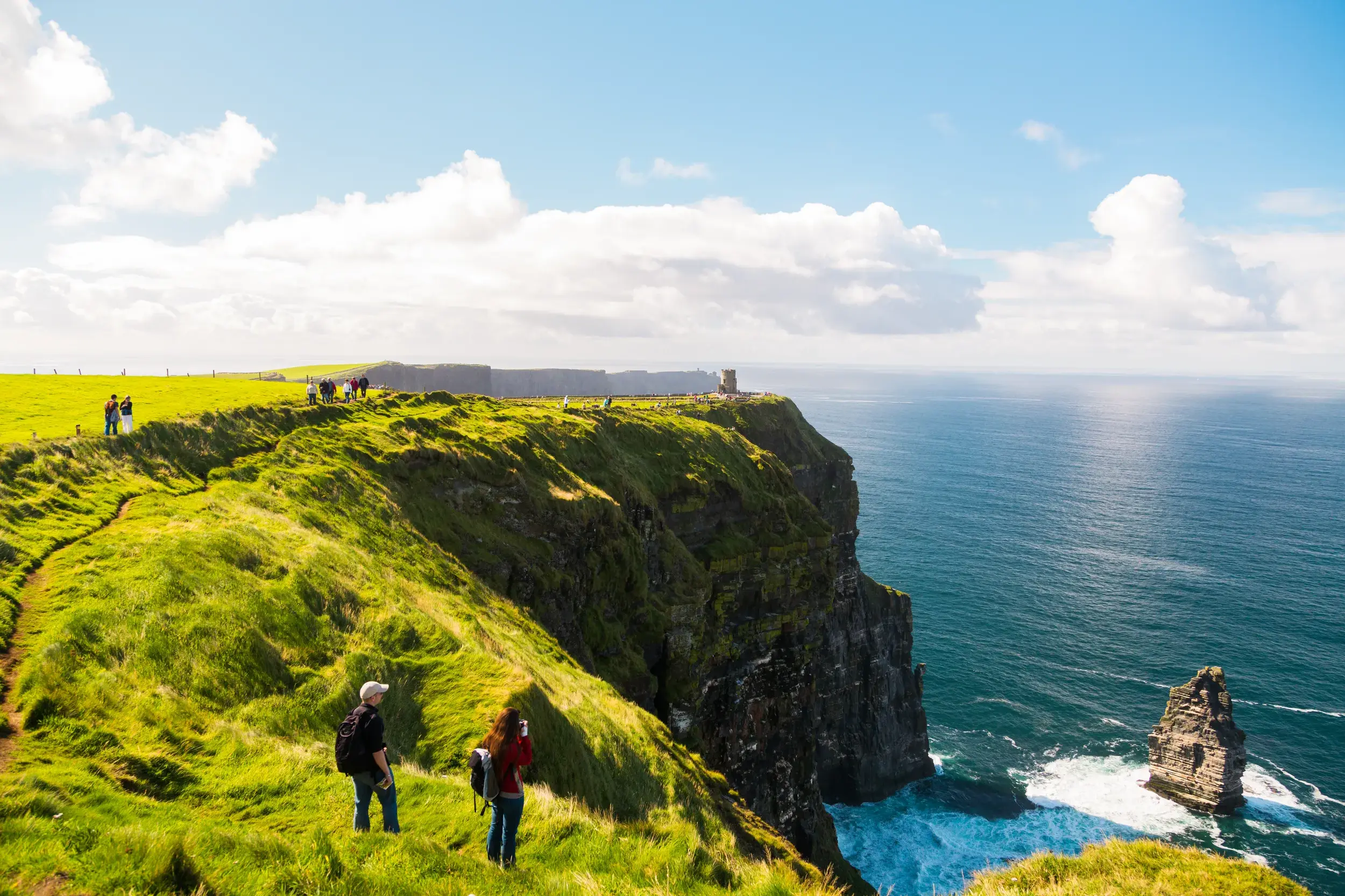 Wanderer auf einer Studienreise entlang der grünen Klippen von Moher mit weitem Blick auf den Atlantik in Irland.