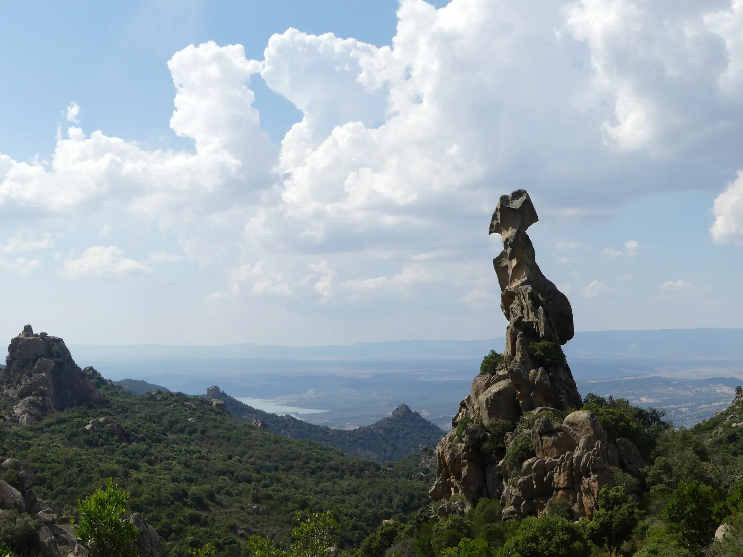 Der markante Granit-Monolith Sa Carbrarissa bei Austis, umgeben von grüner Macchia und mit Weitblick über einen Stausee Sardiniens.