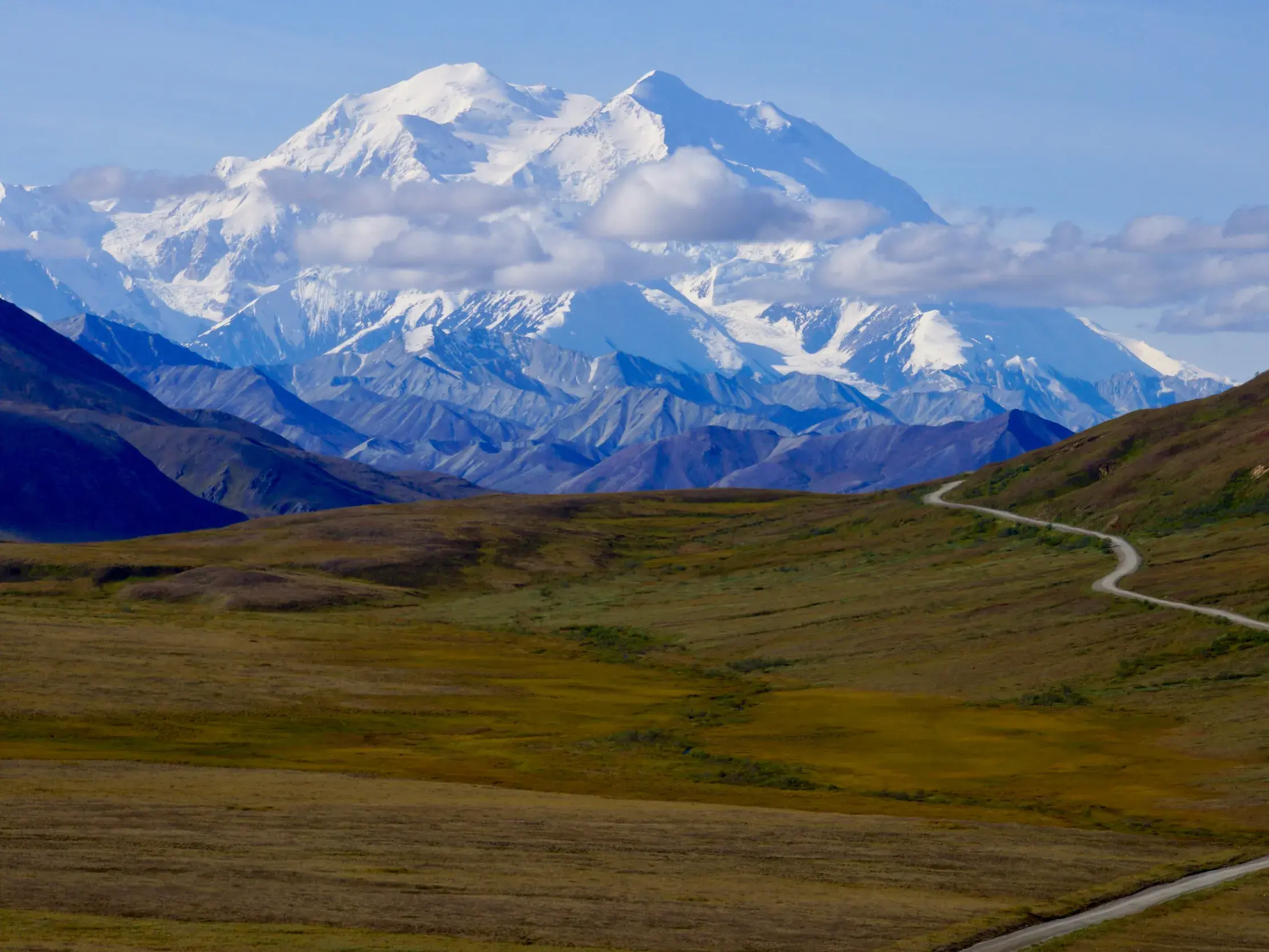 Eine Schotterpiste schlängelt sich durch die Tundra des Denali Nationalparks zum schneebedeckten Mount Denali in Alaska.