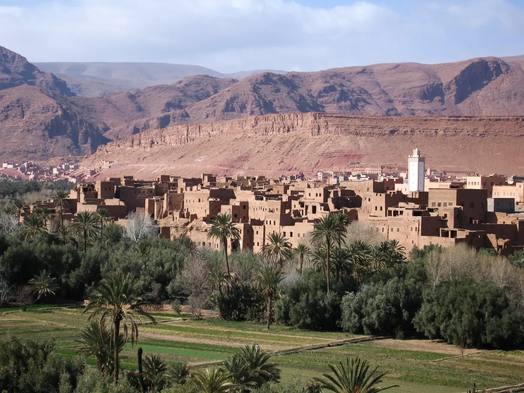 Panoramablick auf eine traditionelle Lehm-Kasbah im grünen Oasental der Dades-Schlucht vor dem Hohen Atlas Gebirge.