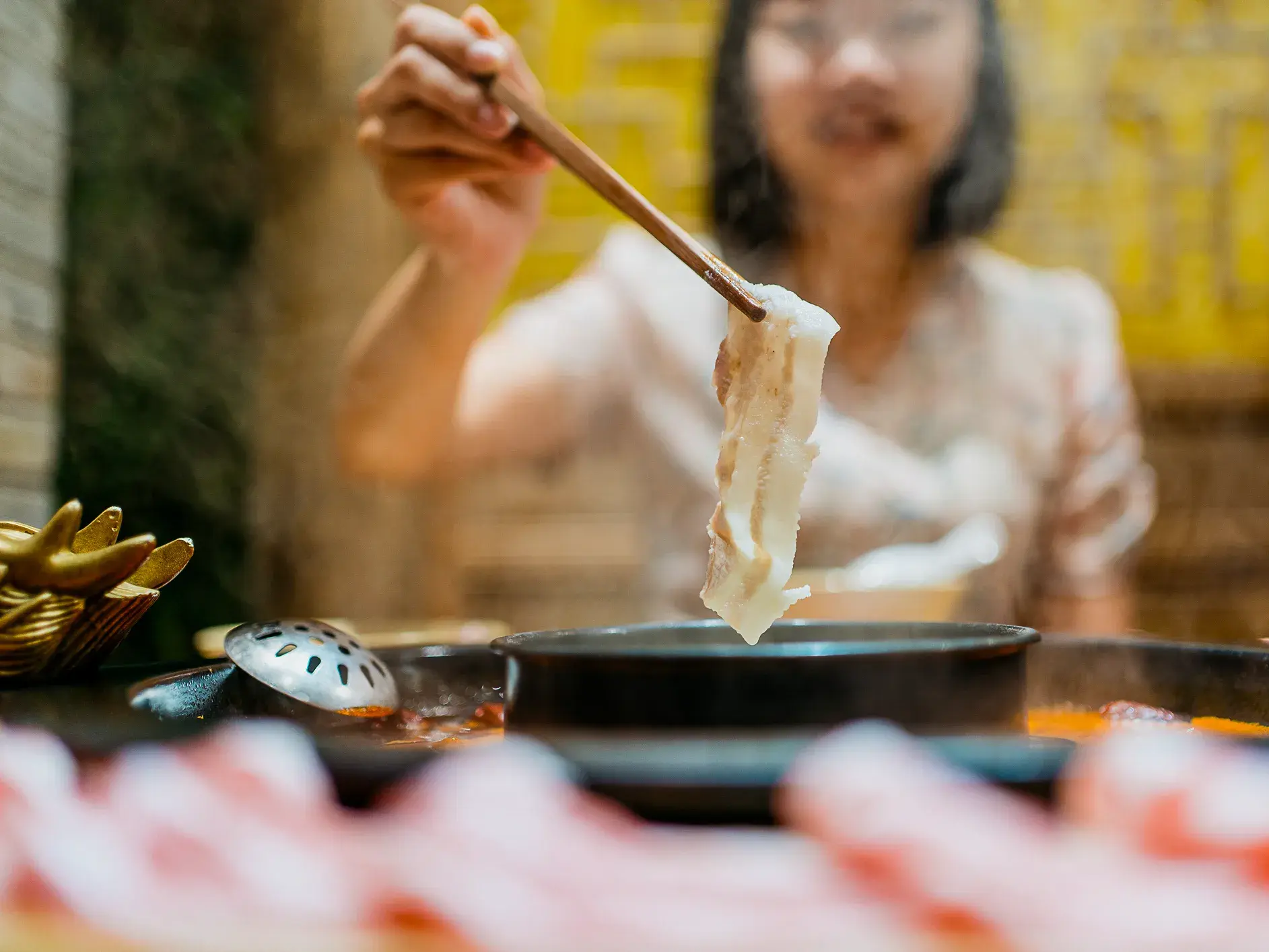 Nahaufnahme von Stäbchen, die Fleisch in einen dampfenden Feuertopf bei einem Spezialitätenessen in Shanghai halten.