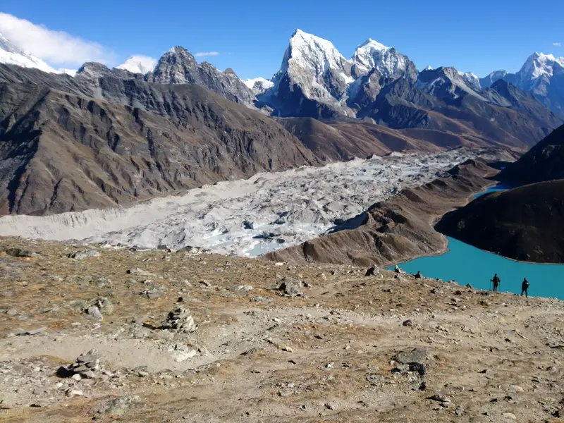 Zwei Wanderer auf dem Gipfel des Gokyo Ri genießen den Blick auf den türkisen Gokyo-See und den gewaltigen Ngozumpa-Gletscher.