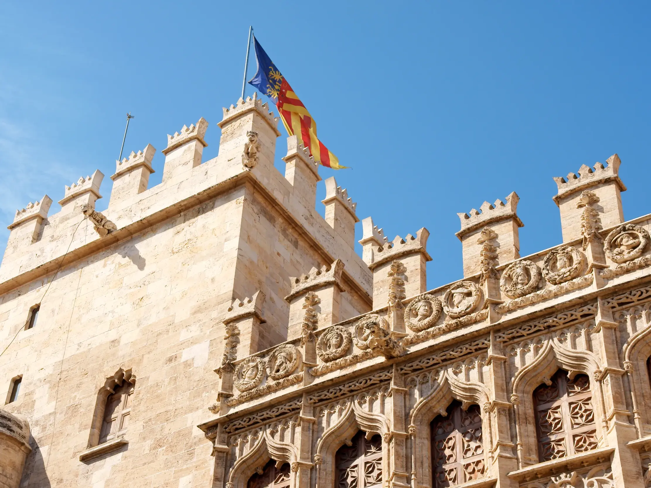 Die valencianische Flagge weht über der gotischen Fassade der Seidenbörse Lonja de la Seda in Valencia bei Sonnenschein.