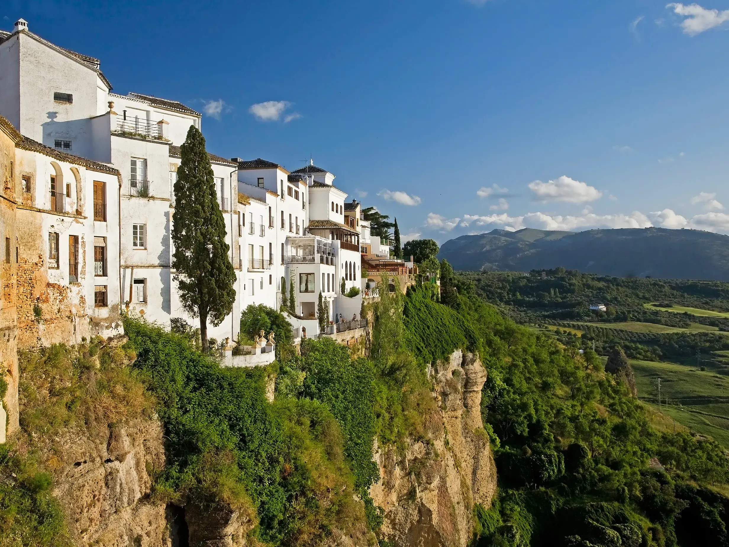 Die berühmten weißen Häuser von Ronda thronen auf dem Felsplateau über der grünen Landschaft Andalusiens bei Sonnenschein.