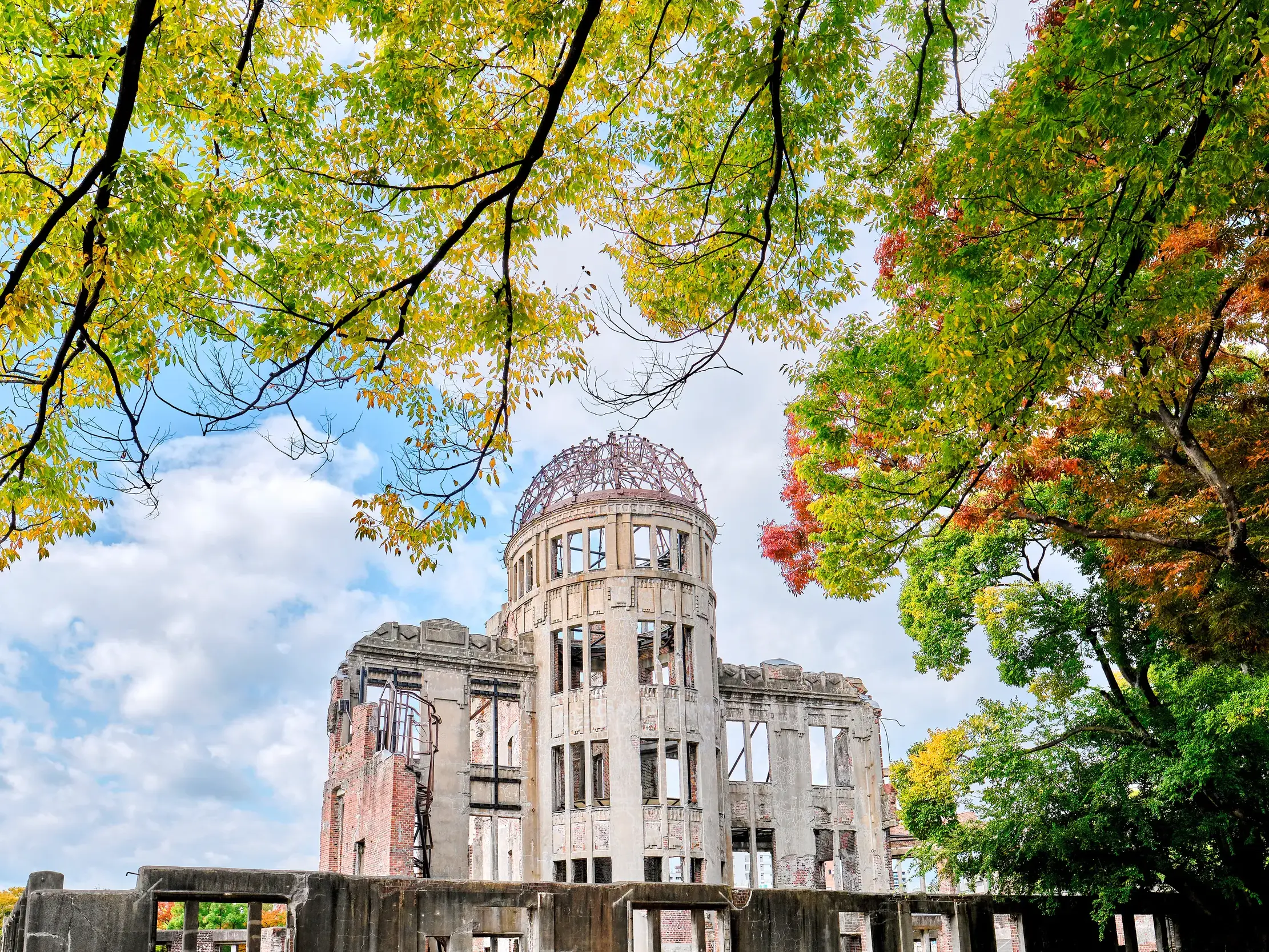 Blick durch herbstlich gefärbte Äste auf den Atombombendom, das Friedensdenkmal im Friedenspark von Hiroshima.