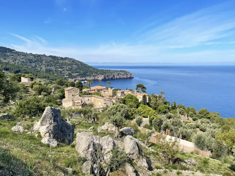 Blick vom Wanderweg GR 221 über Felsen und Olivenhaine auf die Küste und das Dorf Deia in der Serra de Tramuntana.