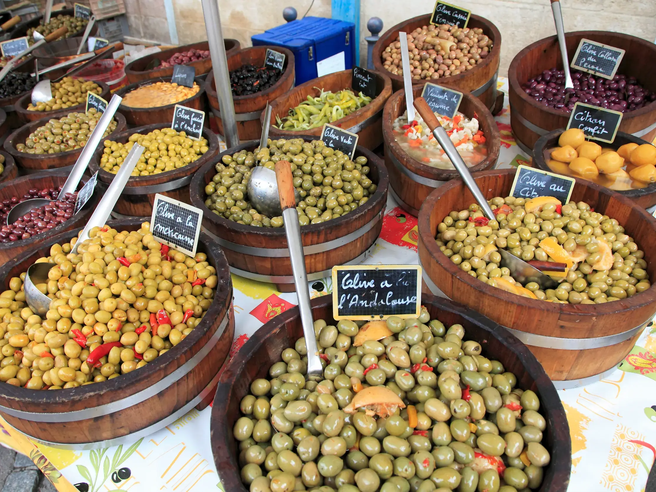 Bunte Vielfalt an eingelegten Oliven und Delikatessen in Holzfässern auf einem Markt in Burgund.