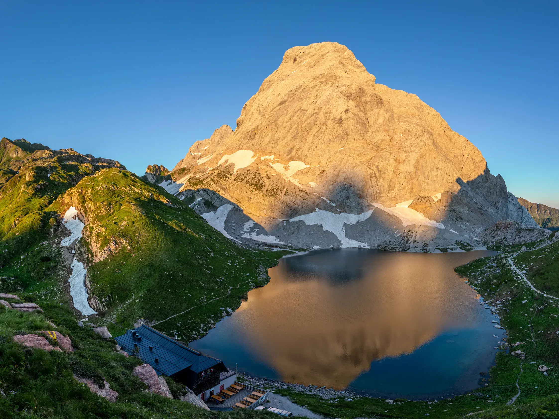 Die von Abendsonne beleuchtete Hohe Warte in den Karnischen Alpen spiegelt sich im Wolayersee vor der Wolayerseehütte.