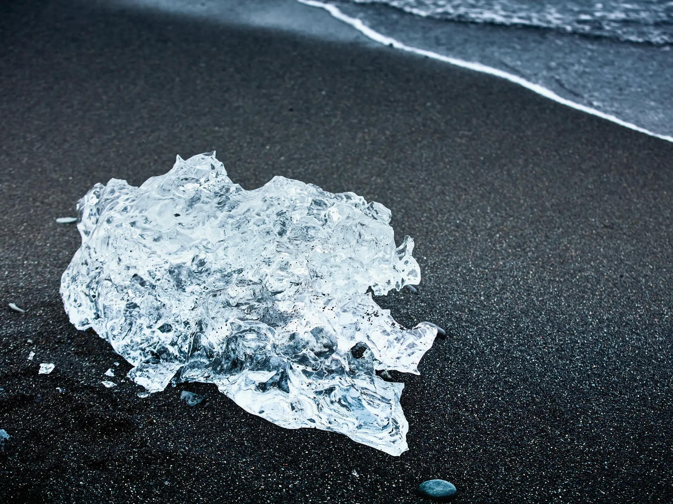 Ein funkelnder Eisdiamant  liegt am schwarzen Vulkansand des Diamond Beach in Island.