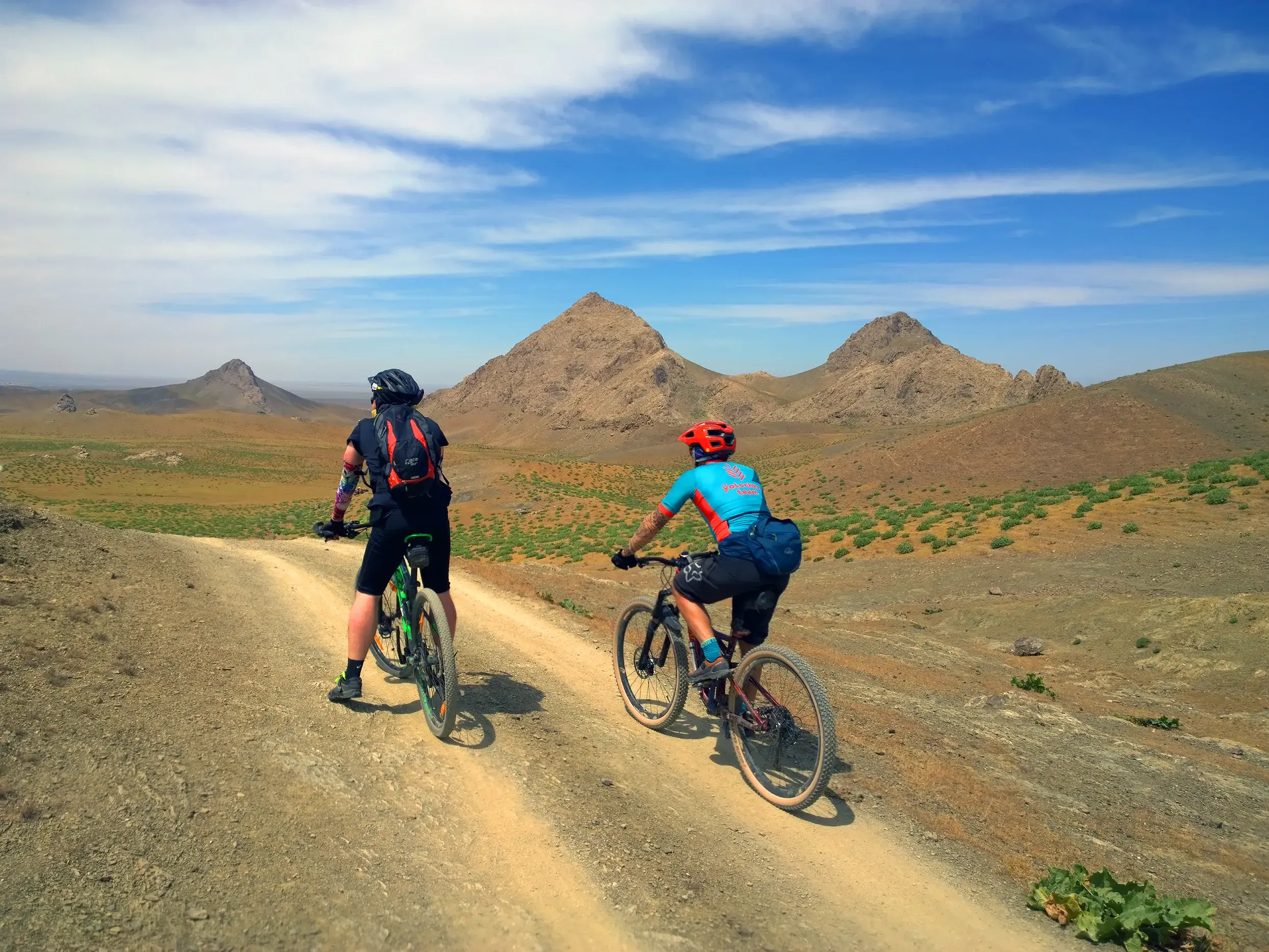 Zwei Mountainbiker auf einer Radreise auf einem Schotterweg durch die karge Berglandschaft des Nuratau-Gebirges in Usbekistan.