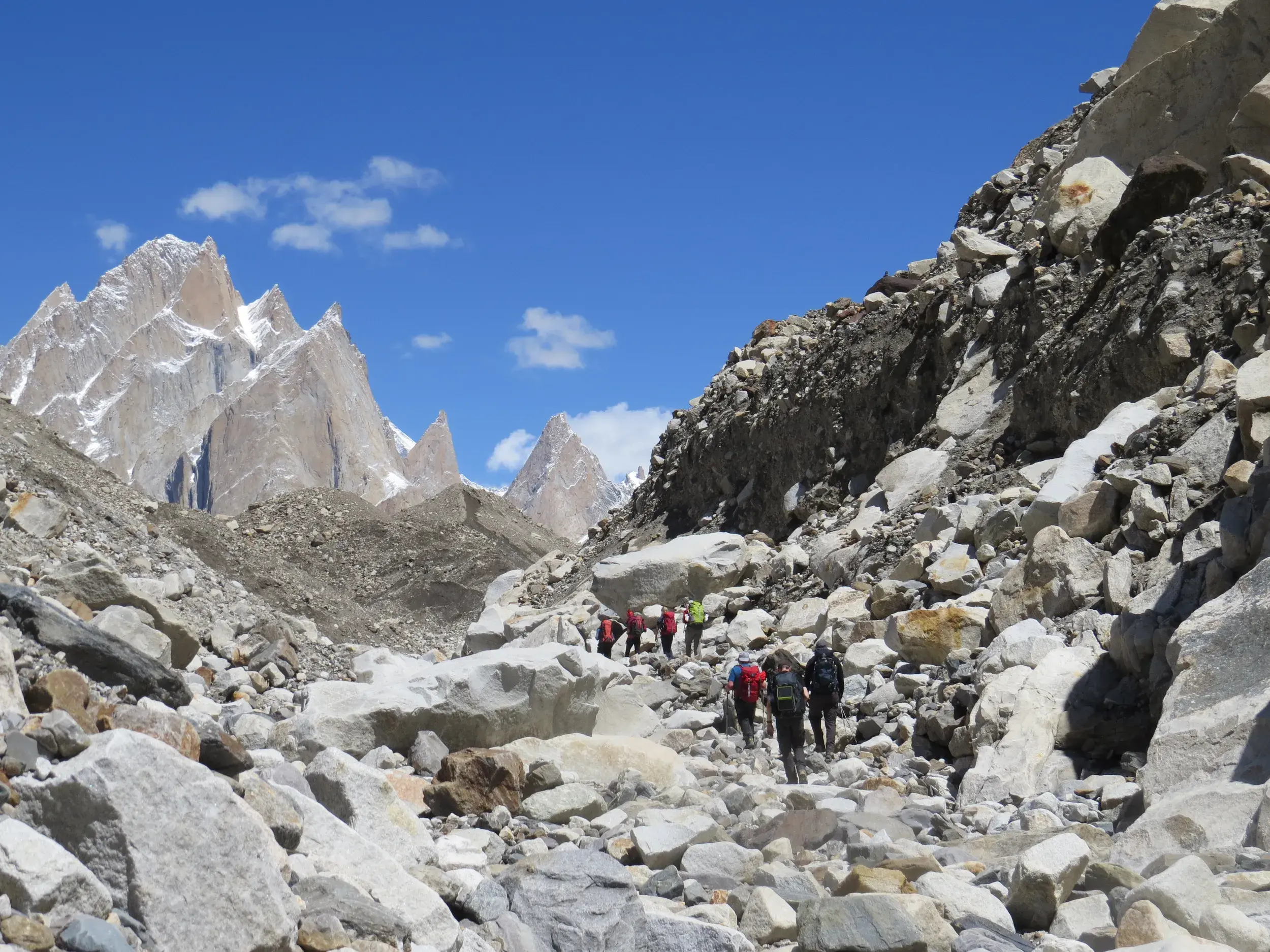 Eine Hauser-Reisegruppe wandert durch ein steiniges Geröllfeld auf dem Baltoro-Gletscher mit den Trango-Türmen im Hintergrund.